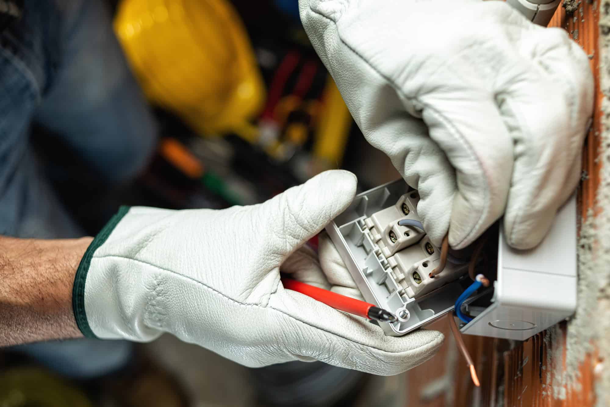 A person wearing protective gloves is wiring an electrical outlet using a screwdriver.