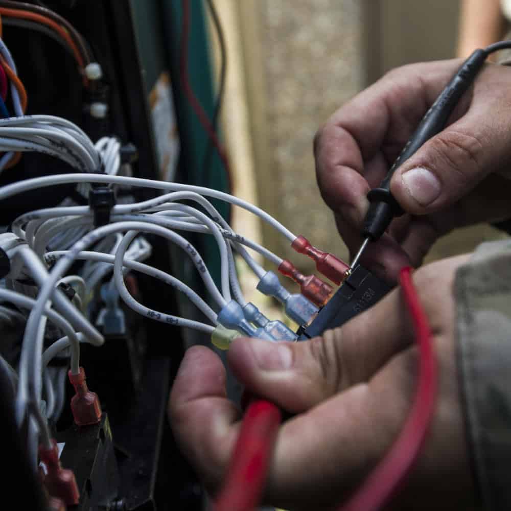 A person is using a multimeter to test electrical connections on a bundle of wires.